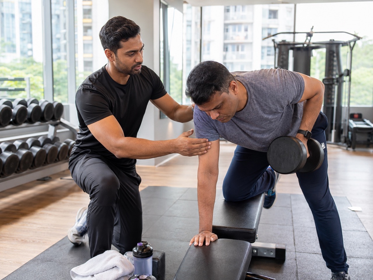 Personal Trainer Correcting Dumbbell Row Technique in Modern Gym | Royalty-Free image | Pixlaris